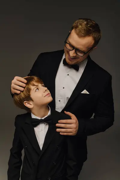 Handsome father and son dressed in tuxedos enjoying a joyful moment together in a studio. — Stock Photo