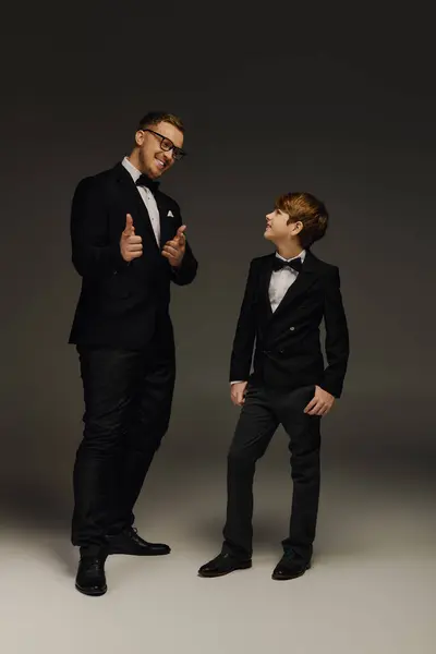 Father and son dressed in stylish tuxedos enjoy a fun, elegant moment in a studio setting. — Stock Photo