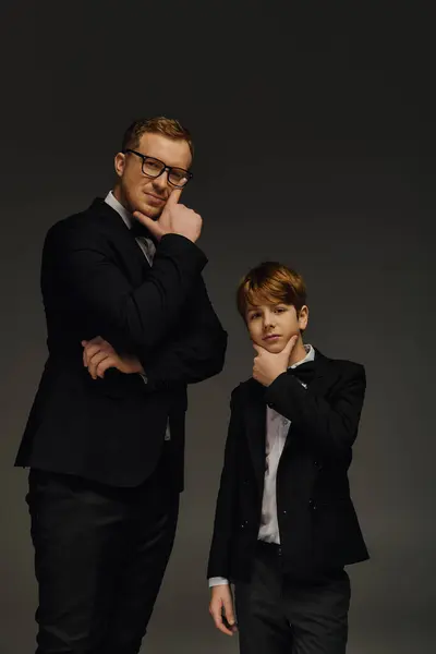 A dapper father and son pose confidently, showcasing their sophisticated bow ties and tuxedos. — Stock Photo