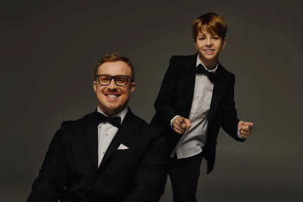 Dressed in elegant tuxedos, a father and son share a delightful moment captured in a studio. — Stock Photo