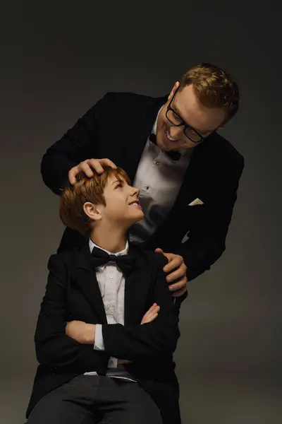 Father and son share a joyful moment in a chic studio, both dressed in elegant tuxedos. — Photo de stock