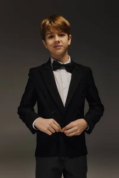 A stylish boy in a tuxedo and bow tie poses confidently in softly lit studio. — Stock Photo