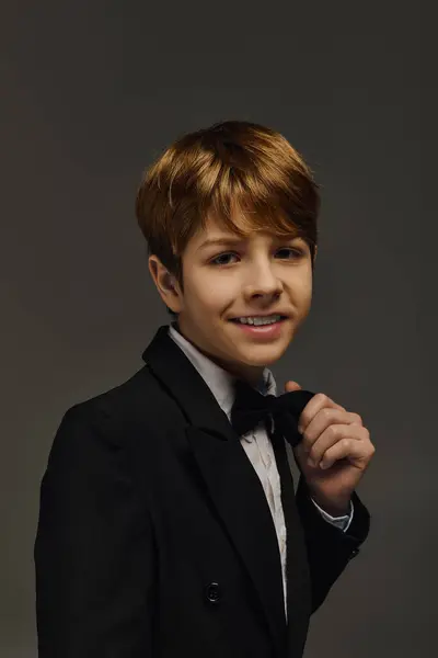 A preteen boy dressed in an elegant tuxedo and bow tie showcases his confident smile in a studio. — Stock Photo