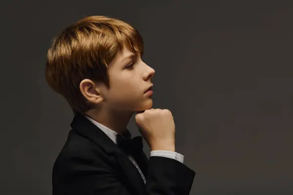 A young boy dressed in a tuxedo with a bow tie gazes thoughtfully while posing in a studio. — Stock Photo