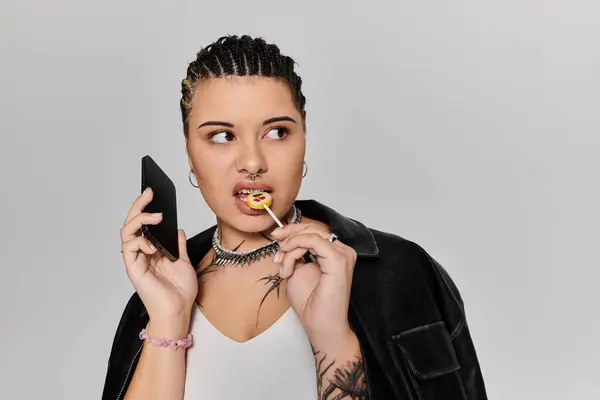 Schicke junge Frau mit Zöpfen hält sich ein Handy ans Ohr und knabbert spielerisch an einem Lutscher. — Stockfoto