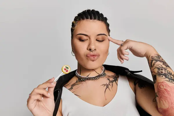 Eine selbstbewusste junge Frau mit kühnen Tätowierungen posiert mit einem Lutscher und stellt ihren einzigartigen Stil zur Schau. — Stockfoto