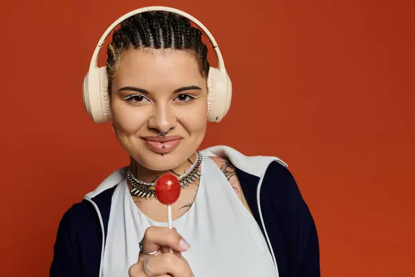 Modische junge Frau lächelt selbstbewusst und hält einen Lutscher mit stylischen Kopfhörern in der Hand. — Stockfoto
