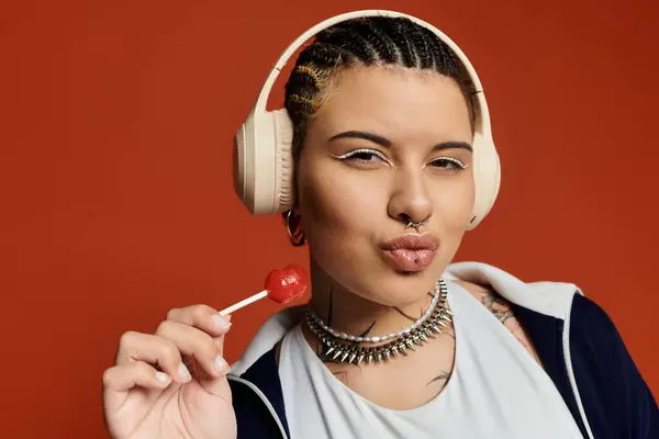 Una giovane donna con trecce e accessori alla moda posa giocosamente con un lecca-lecca e cuffie. — Foto stock