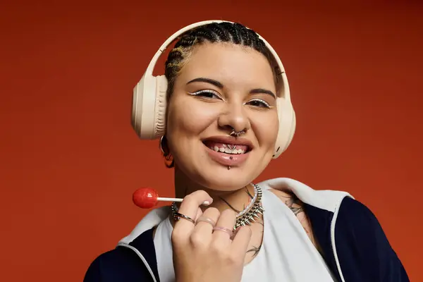 Eine junge Frau mit Zöpfen lächelt, hält einen Lutscher in der Hand und trägt Kopfhörer, verloren in der Musik. — Stockfoto