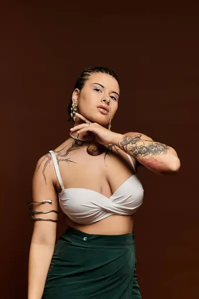 Confident young woman in trendy attire poses elegantly against a brown backdrop, expressing style. — Stock Photo