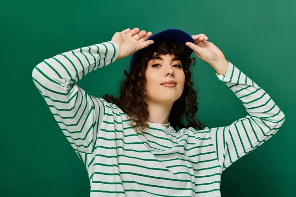 Stylish woman with curly hair showcases her emotions while adjusting her hat in a bright setting. — Stock Photo