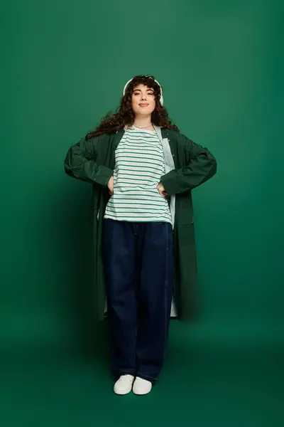 Confident young woman poses with hands on hips, flaunting her stylish outfit in a green setting. — Stock Photo