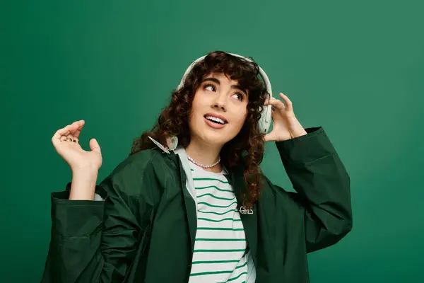 A stylish young woman joyfully wears headphones against a vibrant green backdrop. — Stock Photo