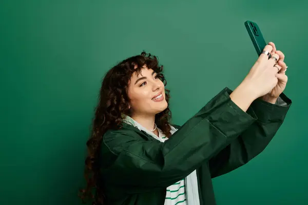 A beautiful woman with curly hair smiles brightly as she captures a moment on her phone. — Stock Photo