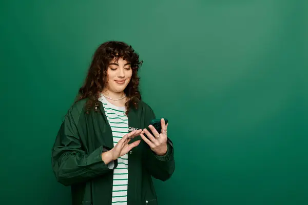 A young woman with curly hair smiles brightly, joyfully interacting with her smartphone. — Stock Photo