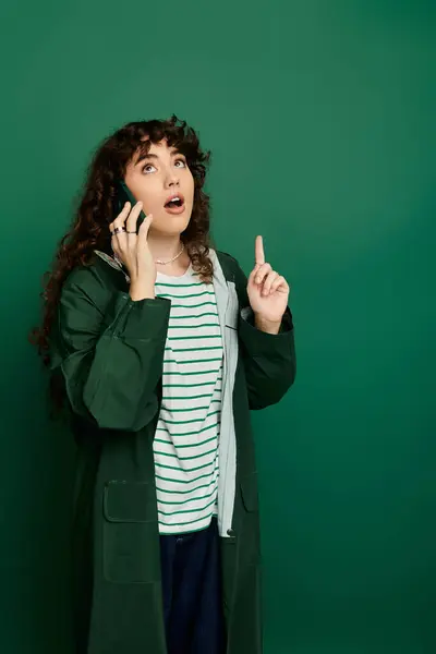 Young woman in stylish clothes enthusiastically gestures on a call against a green backdrop. — Stock Photo