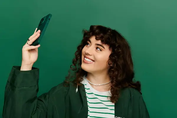 Stylish young woman with curly hair captures a joyful moment with her phone, radiating happiness. — Stock Photo