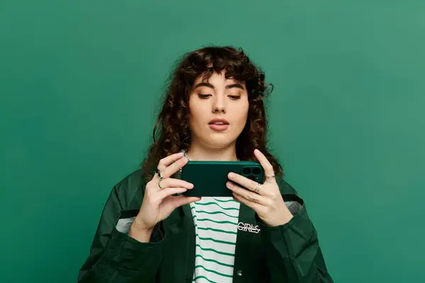 Young woman with curly hair shows emotions on her smartphone against a colorful backdrop. — Stock Photo