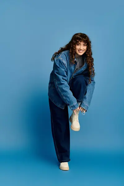 Emozionale giovane donna mette in mostra il suo stile alla moda mentre posa giocosamente su sfondo blu. — Foto stock
