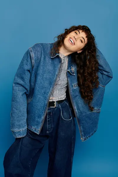 Una mujer joven con el pelo rizado muestra su estilo emocional mientras usa ropa de mezclilla de moda. - foto de stock