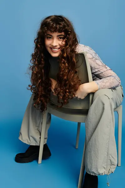 A young, trendy woman with curly hair is joyfully embracing a chair, exuding playful energy. — Stock Photo