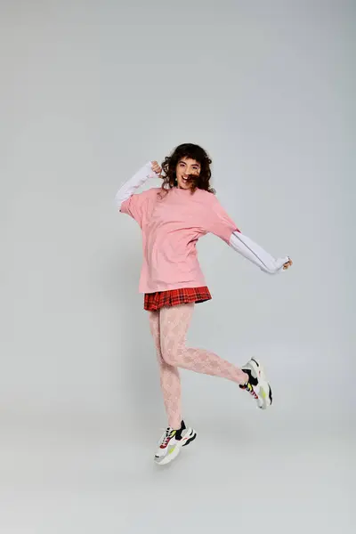 Stylish young woman leaps joyfully, highlighting her chic outfit and vibrant energy in a studio. — Stock Photo