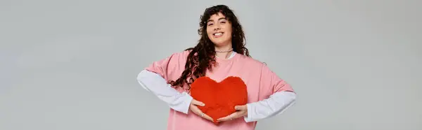 A fashionable young woman expresses joy while holding a red heart shaped decoration in her hands. — Stock Photo