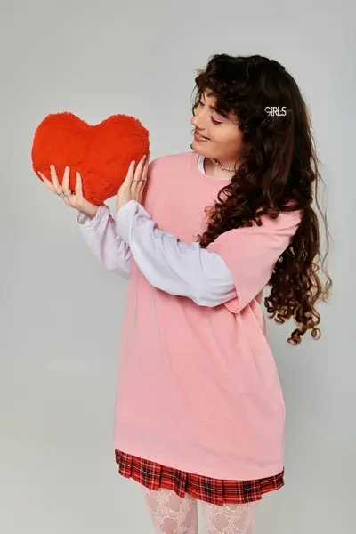 Young woman with curly hair joyfully embraces a red fluffy heart while showcasing her trendy style. — Stock Photo