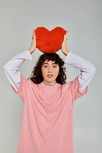 A young woman in a trendy outfit holds a red heart cushion, expressing her emotions. — Stock Photo