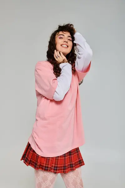 Emotional young woman smiles brightly while posing in a fashionable pink top and plaid skirt. — Stock Photo