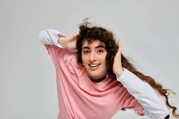 A young woman with curly hair smiles brightly while playfully holding her hair in a modern studio. — Stock Photo
