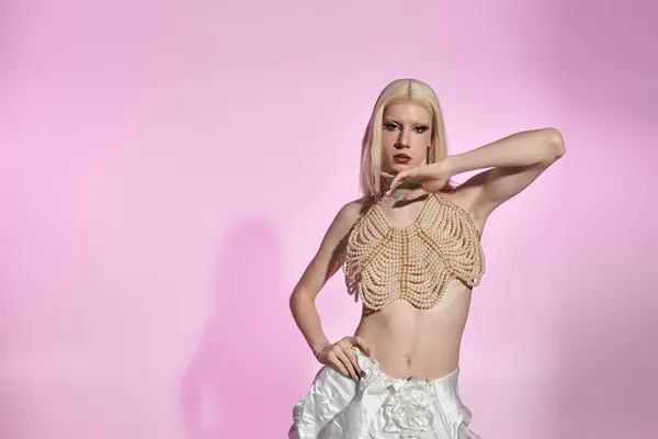 A stylish young drag queen poses in a beaded outfit against a pastel pink background. — Stock Photo