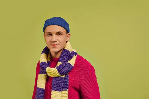Un giovane uomo elegante si erge con fiducia in uno studio decorato con abiti invernali colorati. — Foto stock