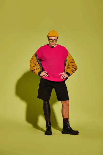 Young man with a prosthetic leg poses confidently in trendy attire against a vibrant backdrop. — Stock Photo