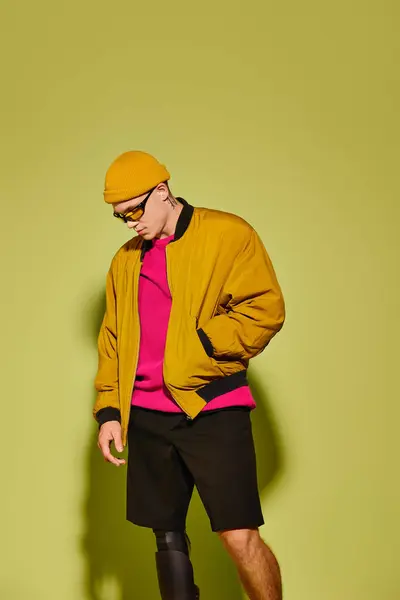 Stylish young man with a prosthetic leg poses in fashionable attire against a green background. — Stock Photo