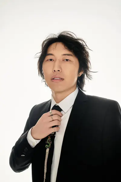 Handsome young asian man dressed in a sharp suit adjusts his tie with confidence and flair. — Stock Photo
