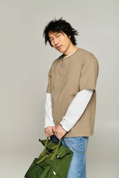Stylish young asian man poses confidently in contemporary fashion while holding a chic bag. — Stock Photo