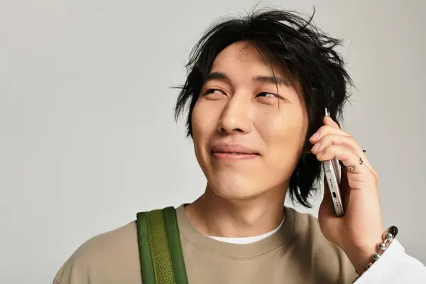 A stylish young Asian man smiles on his phone, reflecting urban youth culture. — Stock Photo