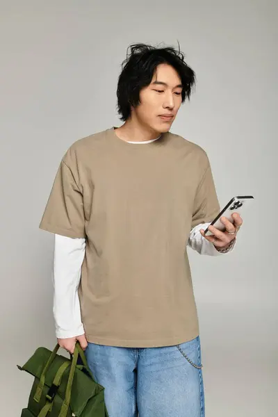 A handsome young asian male stands confidently, checking his phone and showcasing trendy fashion. — Stock Photo