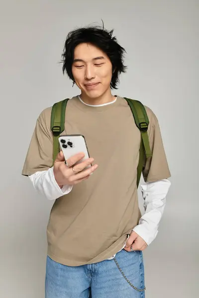 A trendy young Asian man smiles with his smartphone, flaunting modern fashion in style. — Stock Photo