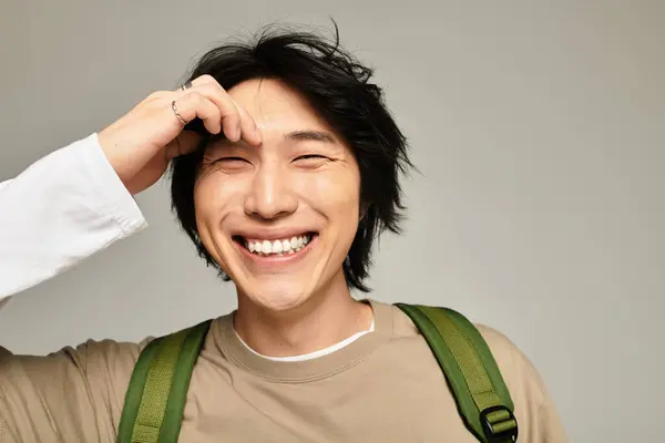 A young and handsome Asian man smiles brightly while playfully running a hand through his hair. — Stock Photo