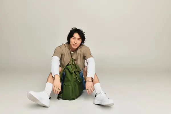 Stylish young man lounges with a trendy green backpack and urban flair. — Stock Photo