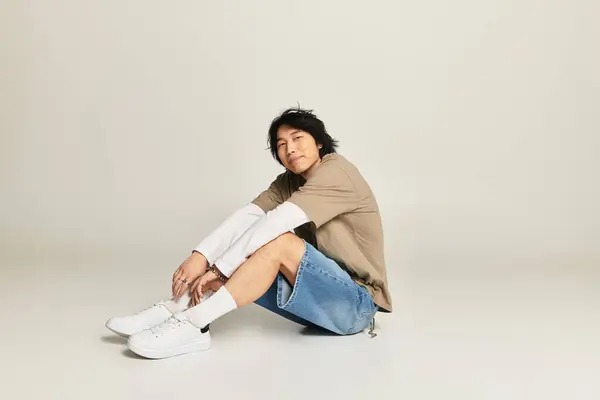 Appealing young asian man sits casually on a smooth surface, embodying youthful fashion trends. — Stock Photo