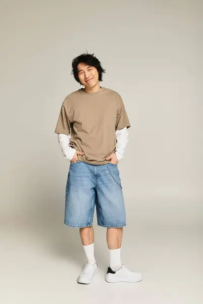 Handsome young asian man stands casually with a charming smile, showcasing his trendy outfit. — Stock Photo