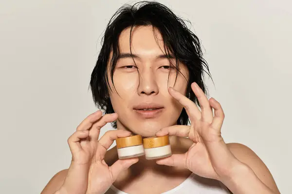 Confident young man poses with skincare jars, reflecting modern youth culture. — Stock Photo