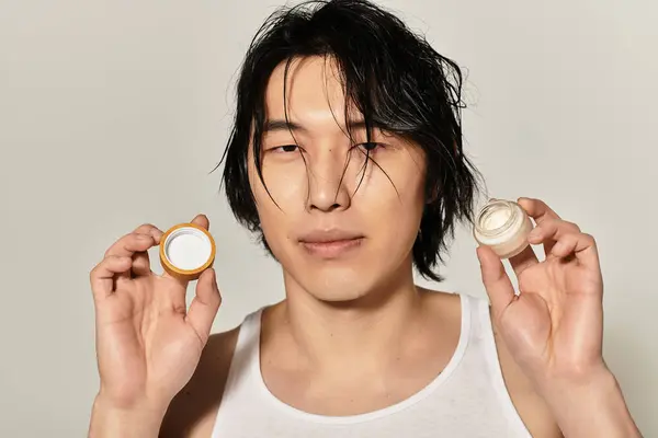 Young man holds skincare jars, emphasizing his stylish look and contemporary grooming routine. — Stock Photo