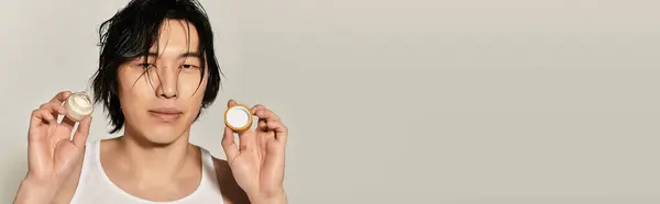 Handsome young man displays fashionable skincare items while posing casually, exuding confidence. — Stock Photo