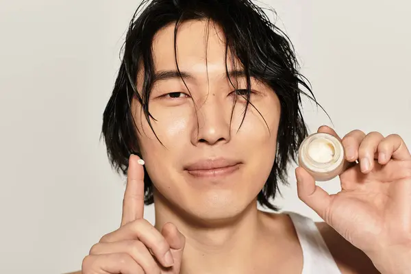 Confident young man smiles with a skincare product, reflecting modern style and youth culture. — Stock Photo
