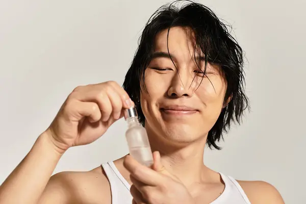 Un joven asiático con estilo felizmente aplica cuidado de la piel, exudando confianza y moda moderna. - foto de stock