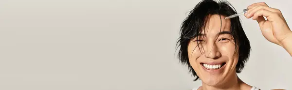 A handsome young asian man has a bright smile as he styles his hair in a trendy urban atmosphere. — Stock Photo
